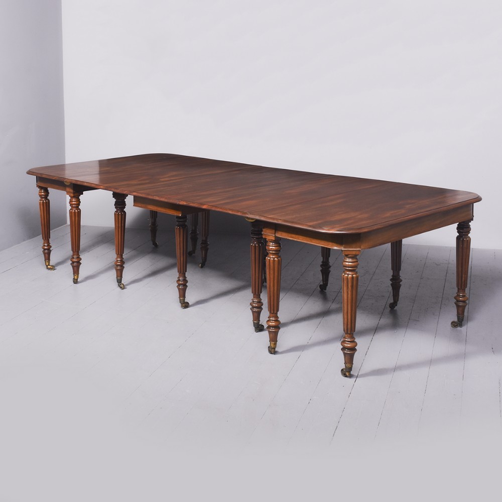A large mahogany extending dining table featuring rounded corners, telescopic extension runners, and reeded turned legs with brass castors.
