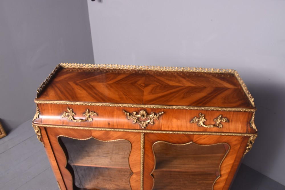 A French kingwood cabinet featuring glazed double doors with shaped panels, decorative gilt-bronze mounts, a brass gallery rail top, and short cabriole legs. View XIII