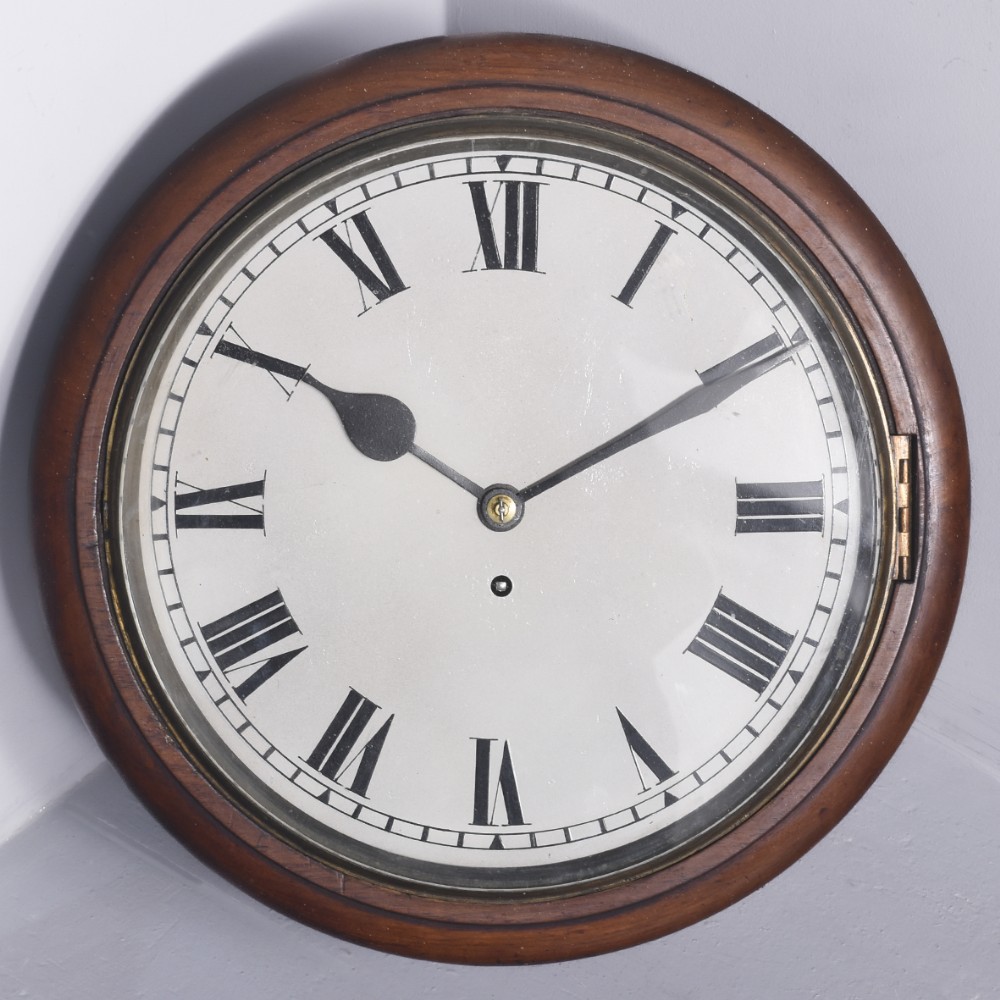 A circular Victorian wall clock featuring a turned mahogany frame surrounding a white dial with black Roman numerals and steel hands.