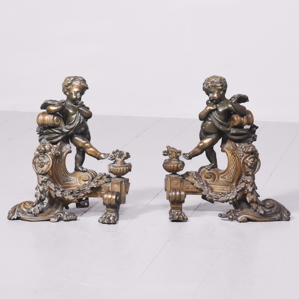 A pair of sculpted dark bronze putti figures mounted on detailed gilded ormolu scroll bases with lion paw feet.