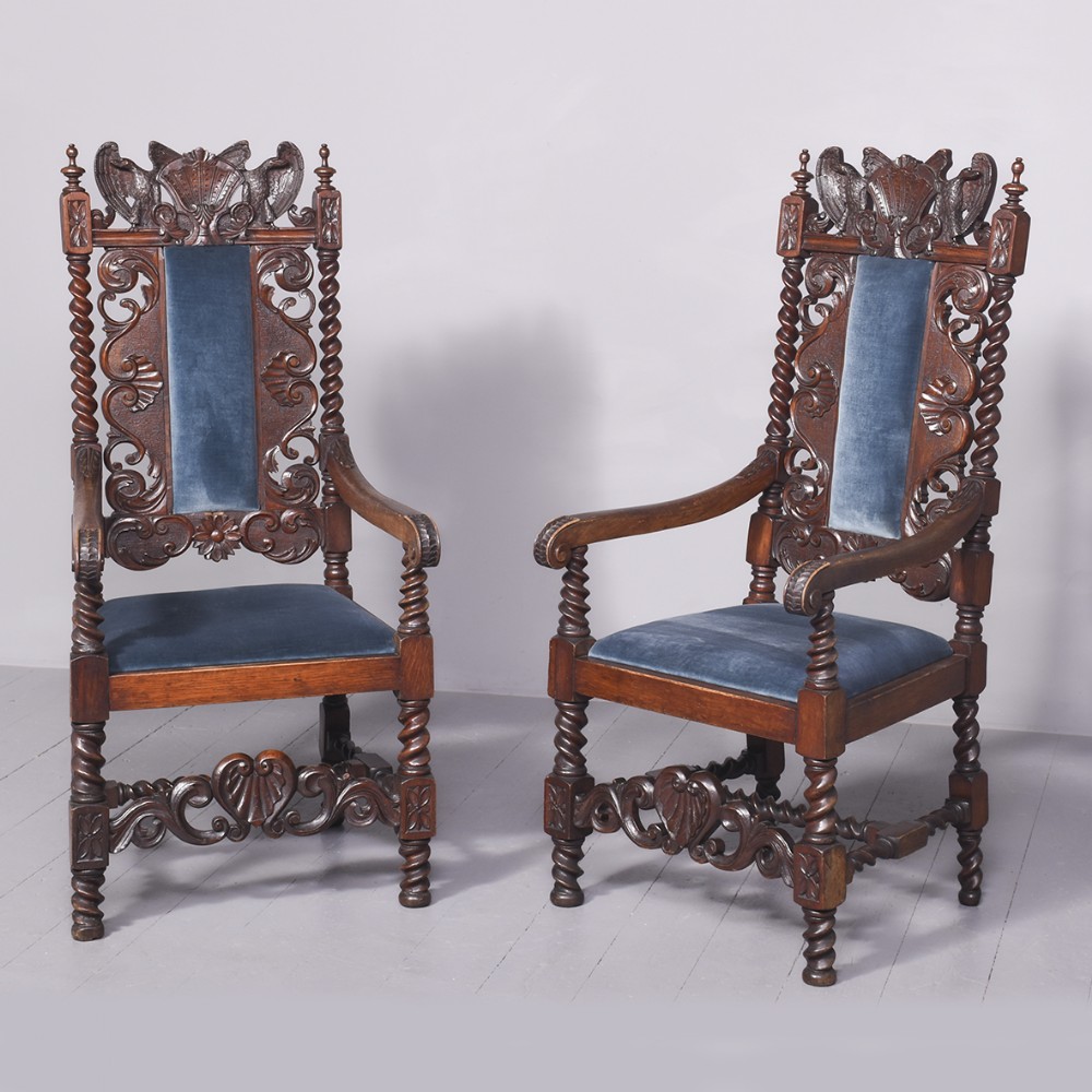 A pair of high-backed carved oak throne chairs featuring blue velvet upholstered panels and seat cushions, barley twist uprights, and carved shell crestings.