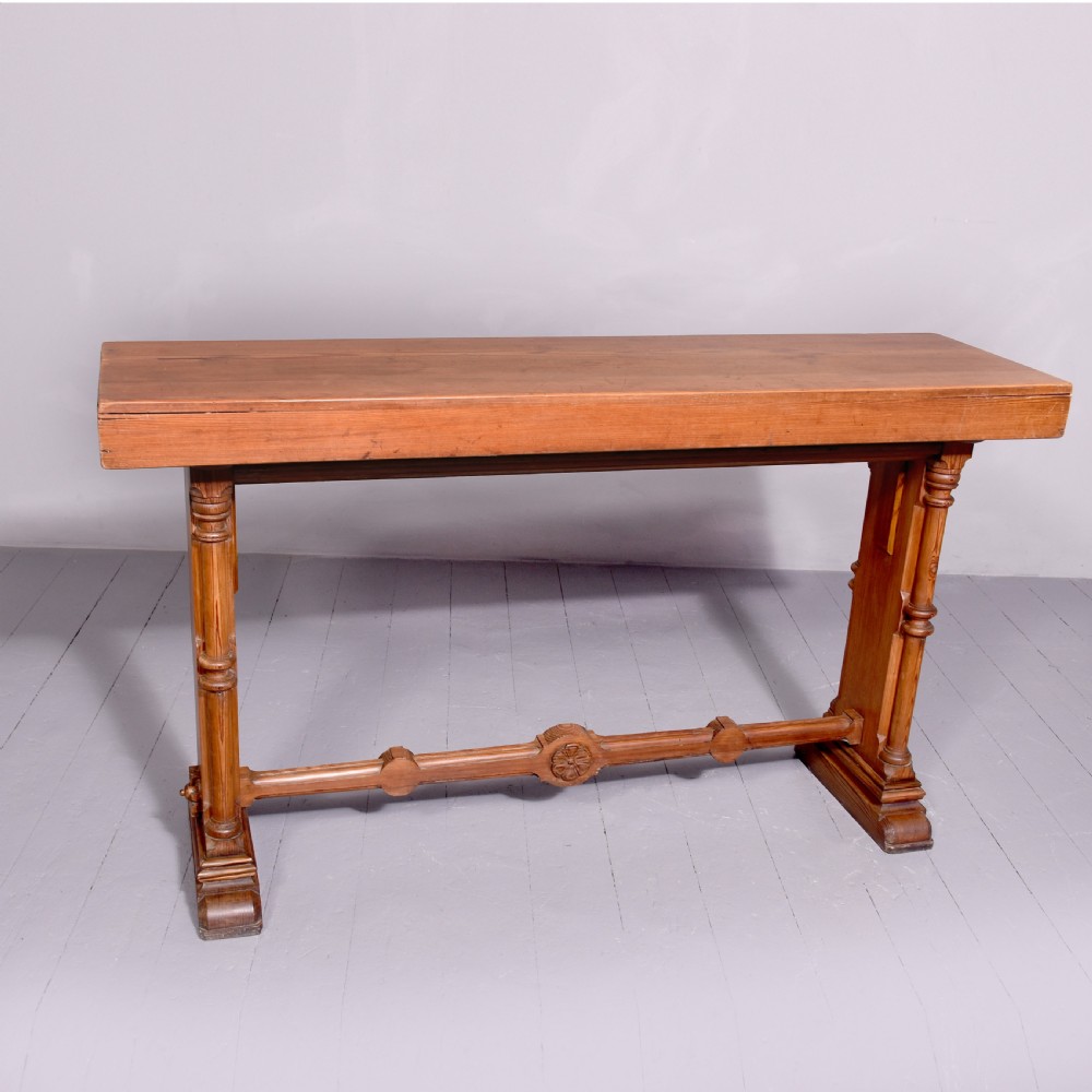 A narrow pitch pine console table featuring a rectangular top, turned twin-column end supports, and a central stretcher with a carved rosette motif.
