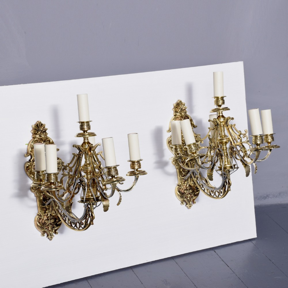 A pair of cast brass Rococo-style five-light wall sconces featuring scrollwork backplates and sweeping candle arms. View V