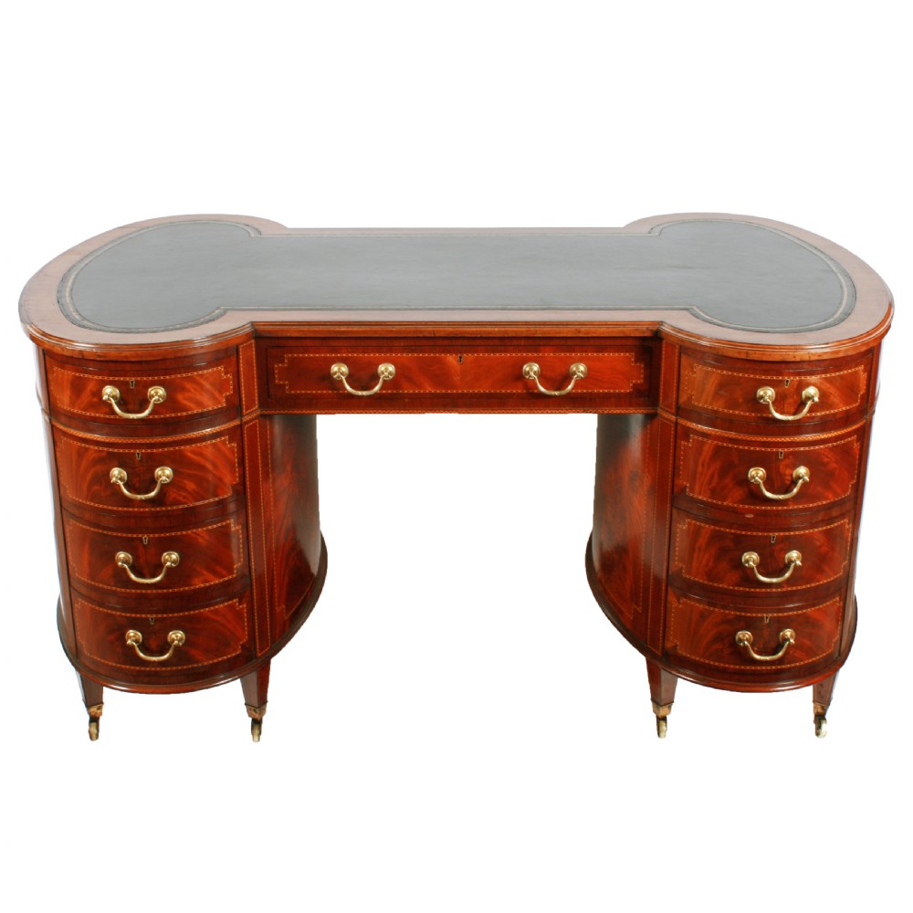 An antique mahogany hourglass-shaped partners desk featuring an inset green leather top, curved drawers with brass handles, and brass castors. View II