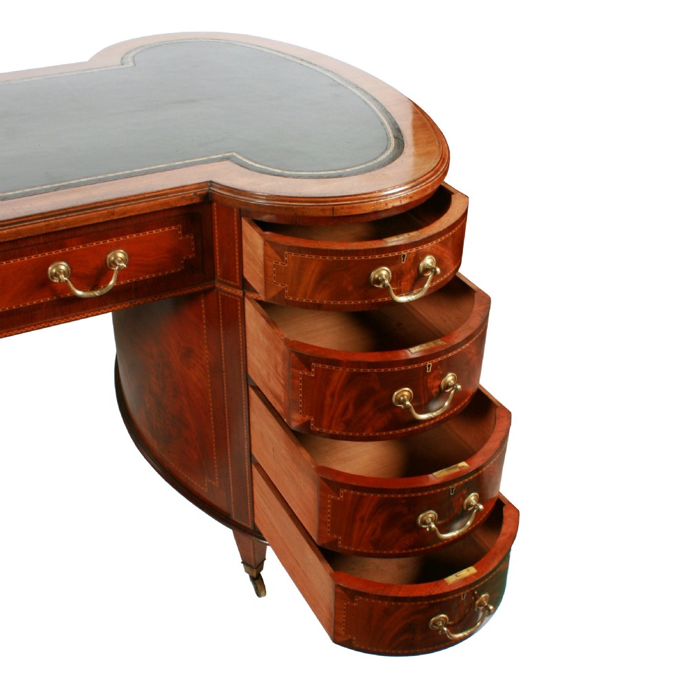An antique mahogany hourglass-shaped partners desk featuring an inset green leather top, curved drawers with brass handles, and brass castors. View V