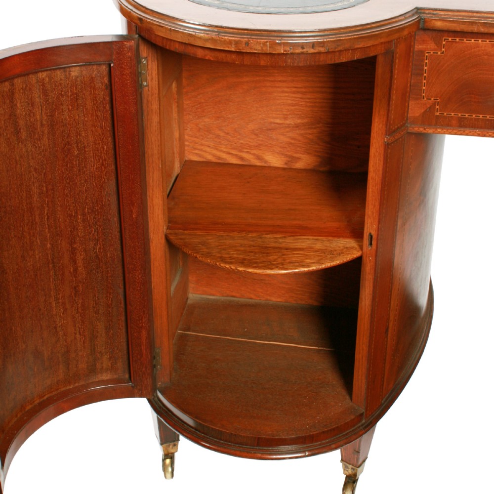 An antique mahogany hourglass-shaped partners desk featuring an inset green leather top, curved drawers with brass handles, and brass castors. View VII