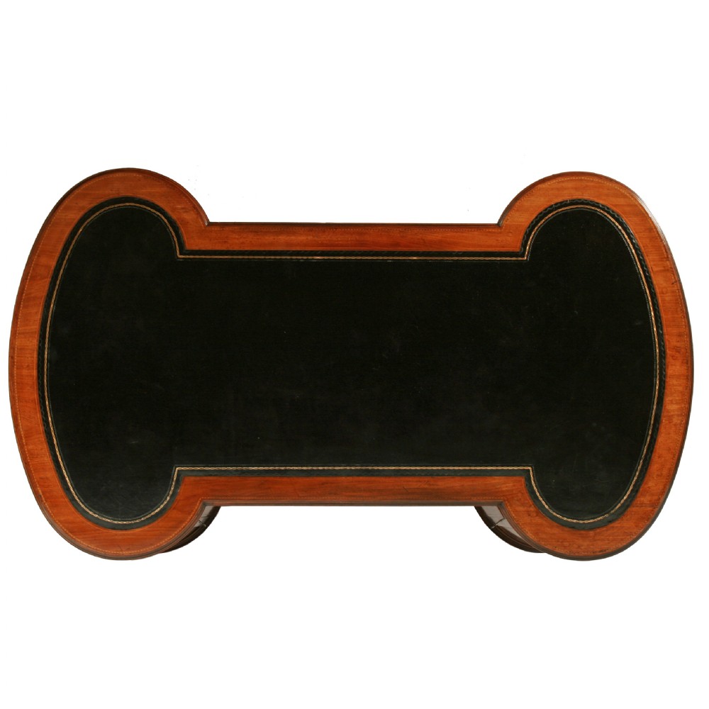 An antique mahogany hourglass-shaped partners desk featuring an inset green leather top, curved drawers with brass handles, and brass castors. View VIII