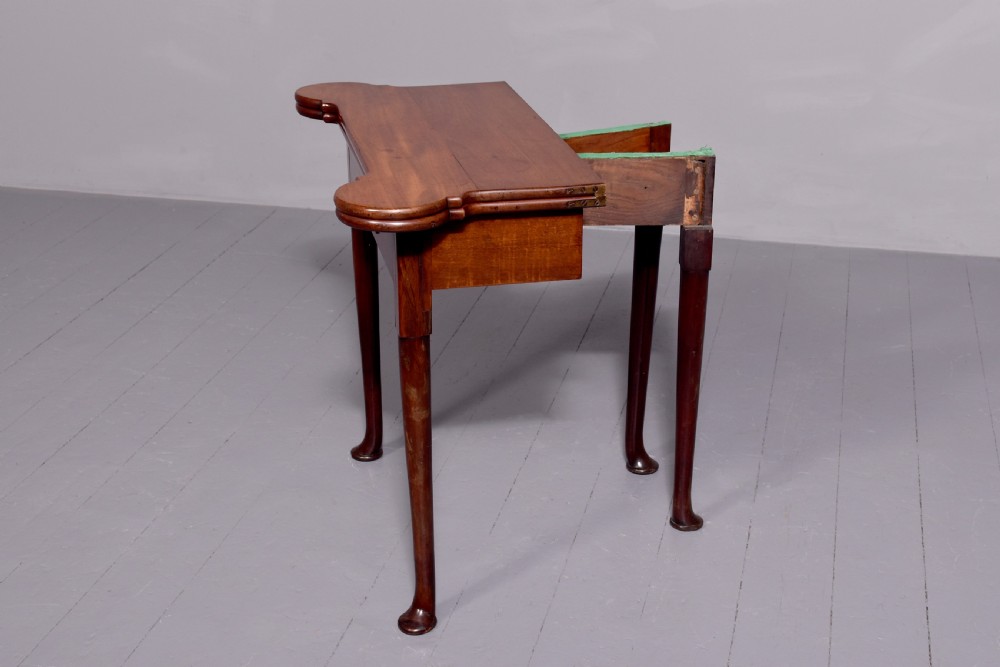 A George II mahogany fold-over games table featuring projecting rounded corners, a central drawer with brass drop handle, and slender legs ending in pad feet. View III