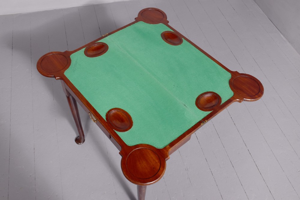 A George II mahogany fold-over games table featuring projecting rounded corners, a central drawer with brass drop handle, and slender legs ending in pad feet. View IV