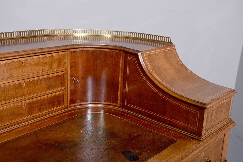 A satinwood Carlton House writing desk featuring a brass gallery railing, U-shaped superstructure with small drawers, leather writing surface, and square tapered legs on castors. View II