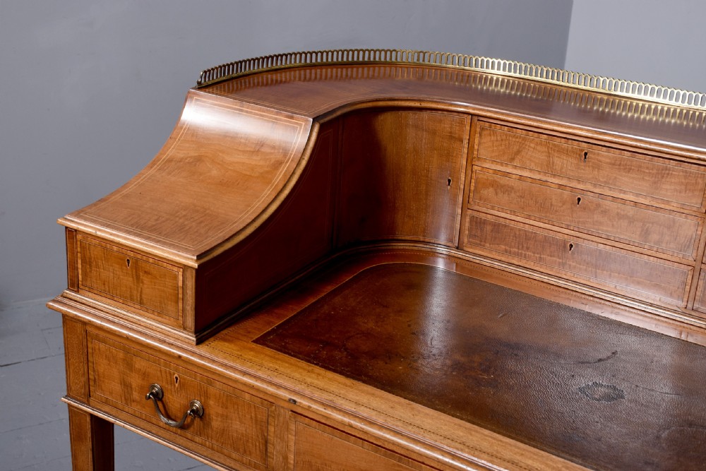 A satinwood Carlton House writing desk featuring a brass gallery railing, U-shaped superstructure with small drawers, leather writing surface, and square tapered legs on castors. View III