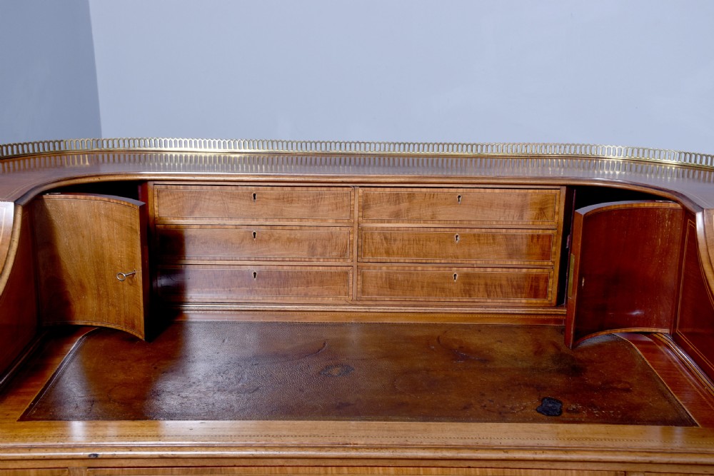 A satinwood Carlton House writing desk featuring a brass gallery railing, U-shaped superstructure with small drawers, leather writing surface, and square tapered legs on castors. View V