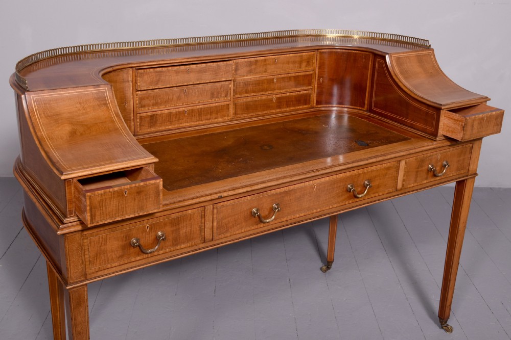 A satinwood Carlton House writing desk featuring a brass gallery railing, U-shaped superstructure with small drawers, leather writing surface, and square tapered legs on castors. View VIII