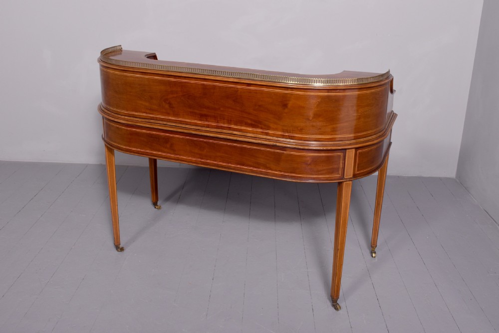 A satinwood Carlton House writing desk featuring a brass gallery railing, U-shaped superstructure with small drawers, leather writing surface, and square tapered legs on castors. View XIII