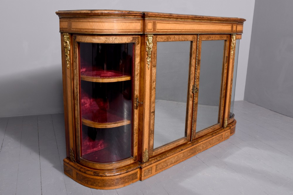 A Mid-Victorian burr walnut and satinwood credenza with mirrored central doors, curved glass side cupboards, and gilt ormolu mounts. View III