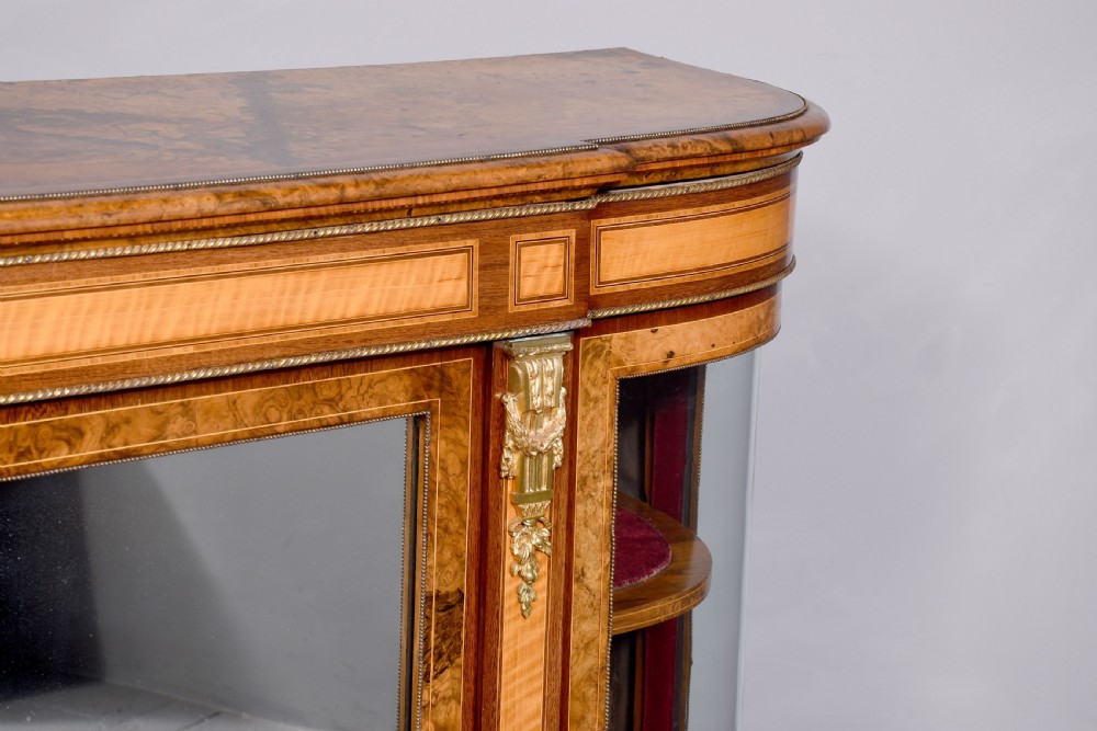 A Mid-Victorian burr walnut and satinwood credenza with mirrored central doors, curved glass side cupboards, and gilt ormolu mounts. View IV