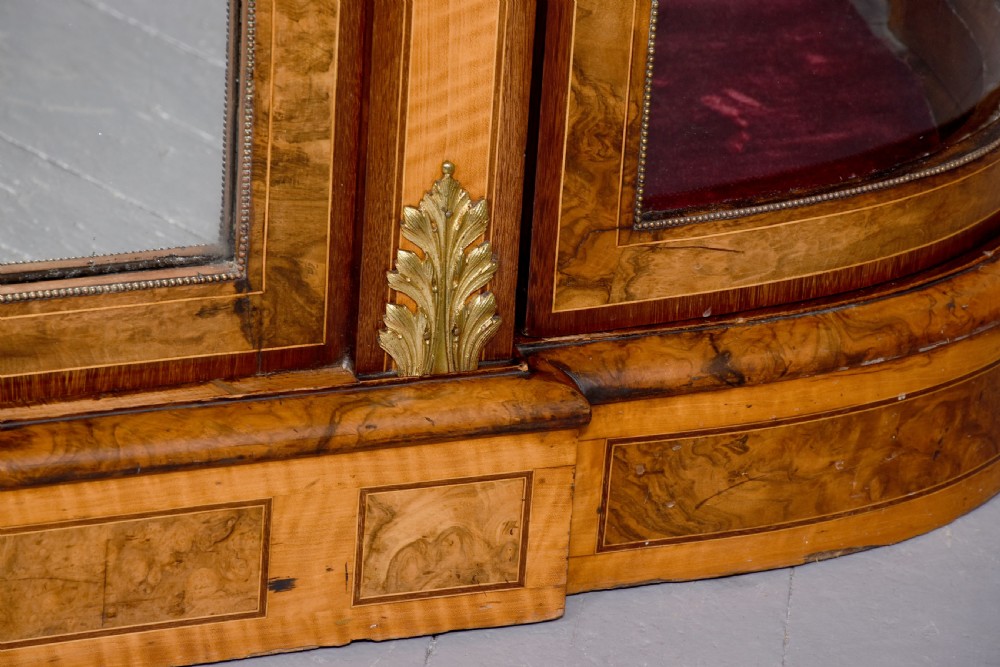 A Mid-Victorian burr walnut and satinwood credenza with mirrored central doors, curved glass side cupboards, and gilt ormolu mounts. View V