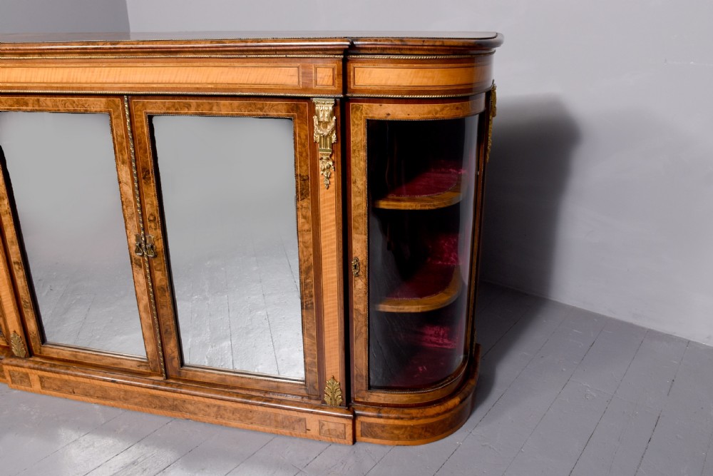 A Mid-Victorian burr walnut and satinwood credenza with mirrored central doors, curved glass side cupboards, and gilt ormolu mounts. View VII
