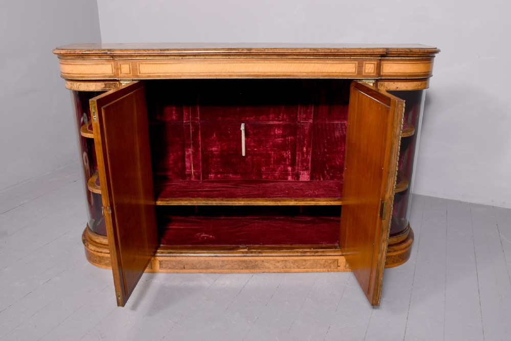 A Mid-Victorian burr walnut and satinwood credenza with mirrored central doors, curved glass side cupboards, and gilt ormolu mounts. View VIII