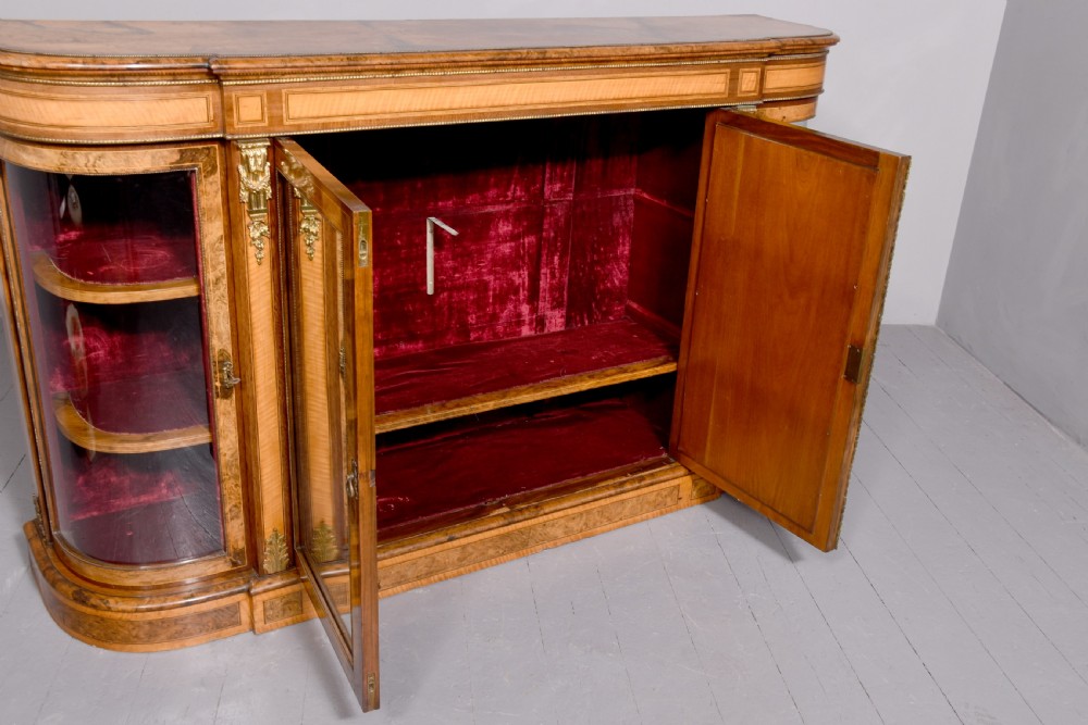 A Mid-Victorian burr walnut and satinwood credenza with mirrored central doors, curved glass side cupboards, and gilt ormolu mounts. View IX