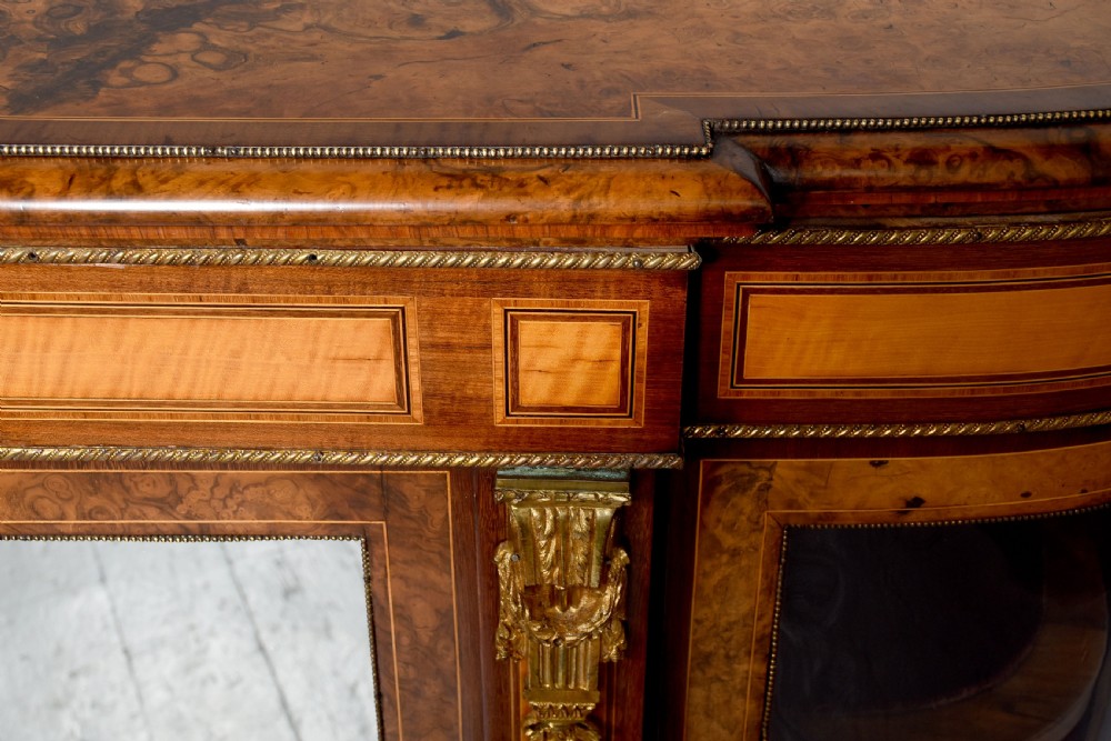 A Mid-Victorian burr walnut and satinwood credenza with mirrored central doors, curved glass side cupboards, and gilt ormolu mounts. View XI