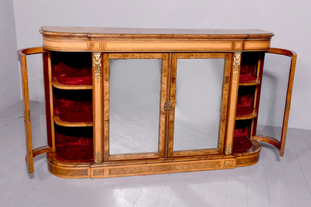 A Mid-Victorian burr walnut and satinwood credenza with mirrored central doors, curved glass side cupboards, and gilt ormolu mounts. View XIII