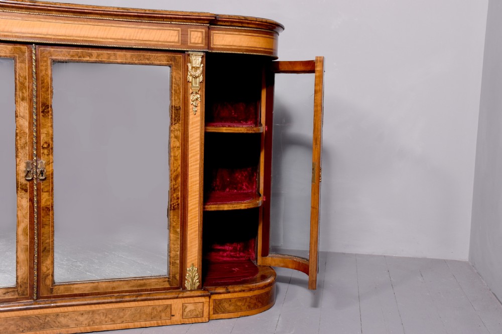 A Mid-Victorian burr walnut and satinwood credenza with mirrored central doors, curved glass side cupboards, and gilt ormolu mounts. View XV