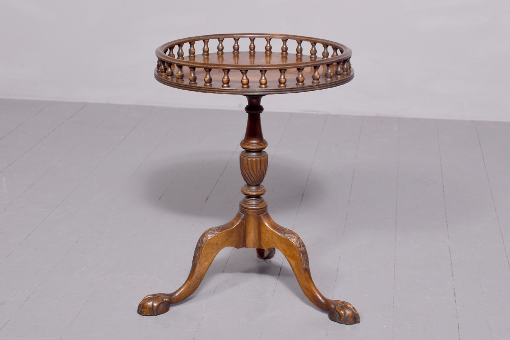 A round mahogany occasional table featuring a raised spindle gallery top, turned central pedestal stem, and cabriole tripod legs ending in claw and ball feet.