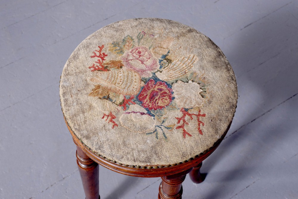 A tall George III circular wooden stool featuring four turned legs, a floral tapestry seat, and brass stud detailing along the rim. View II