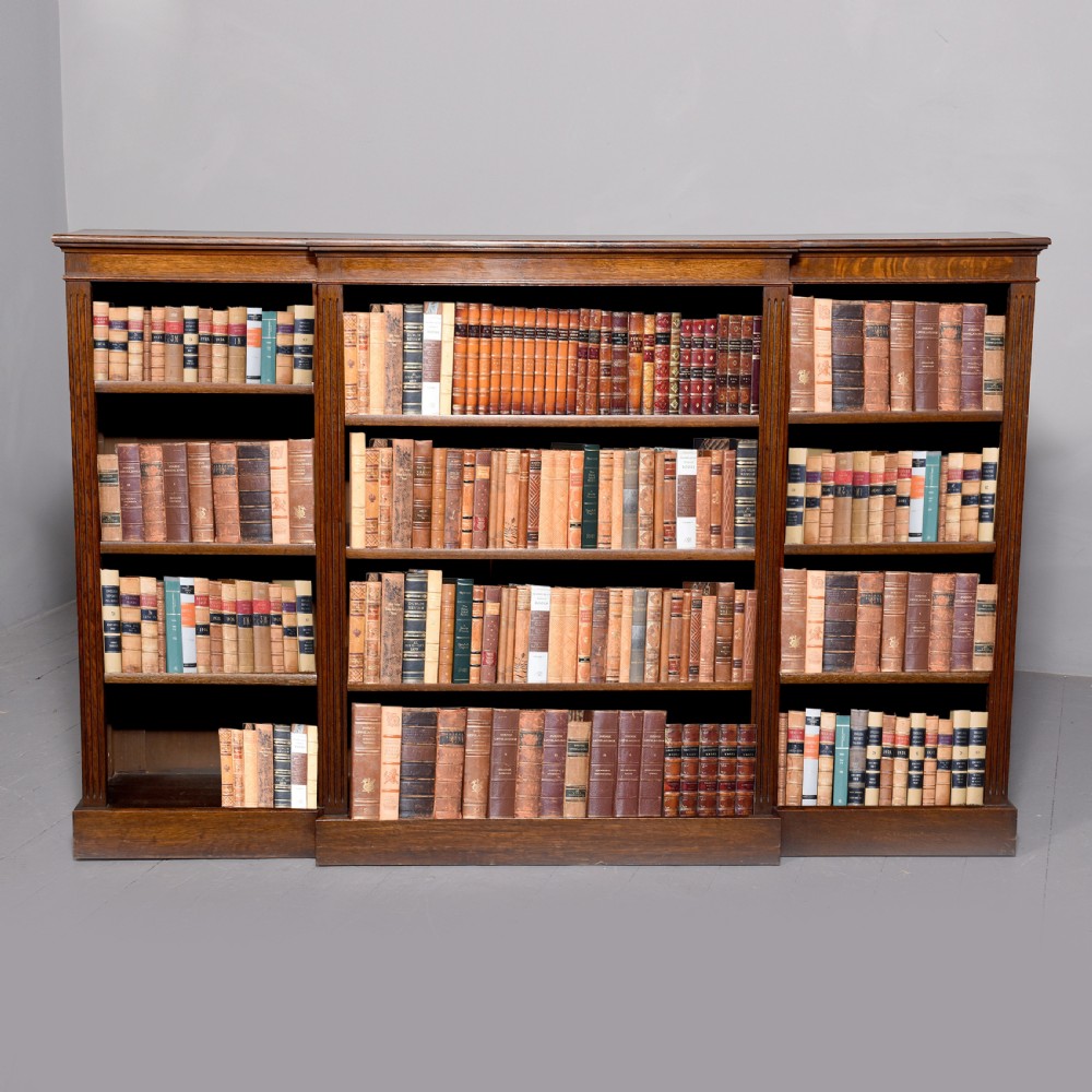 A large dark oak breakfront open bookcase filled with rows of leather-bound books.