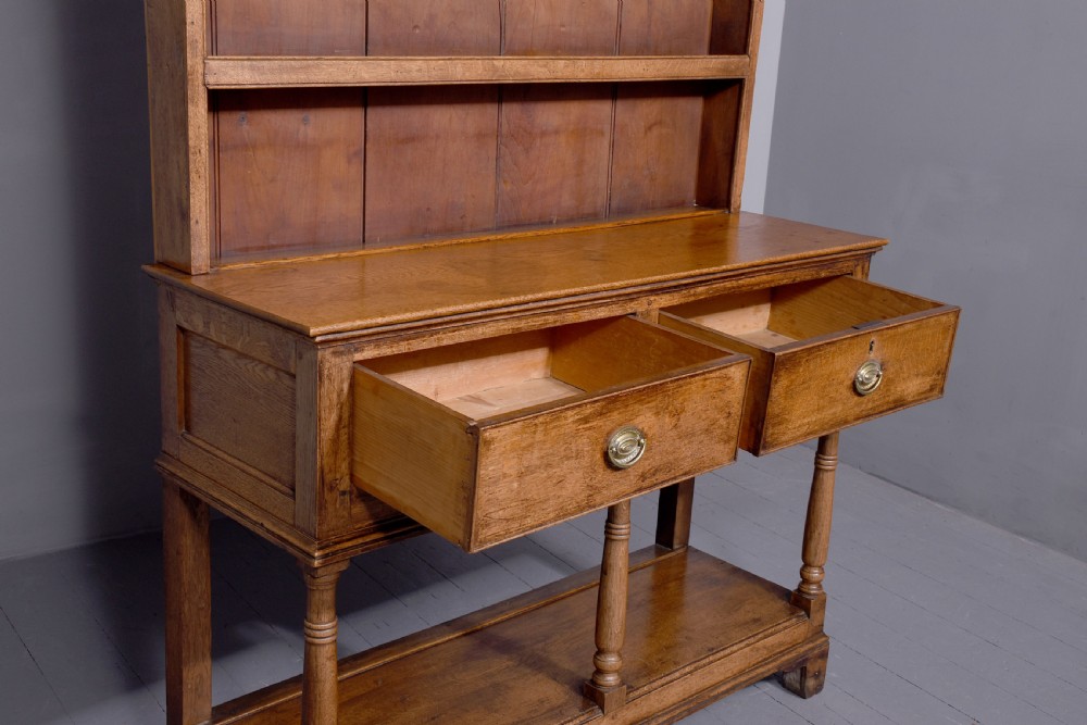 A George III two-part oak dresser featuring an open three-shelf plate rack with iron hooks above two drawers and an open potboard base. View IV