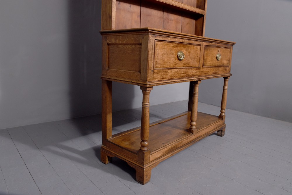 A George III two-part oak dresser featuring an open three-shelf plate rack with iron hooks above two drawers and an open potboard base. View V