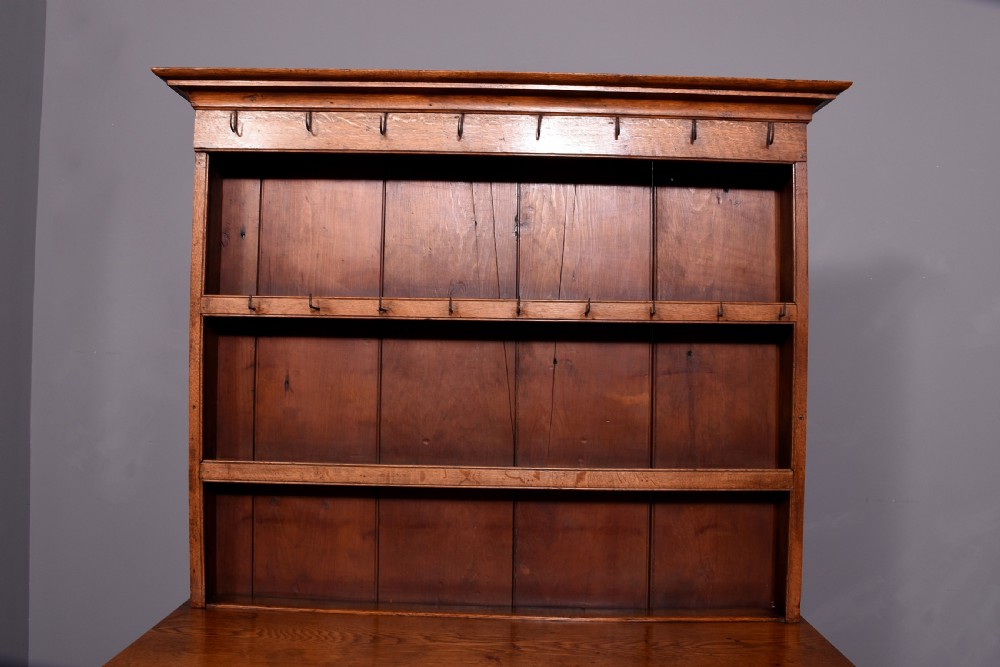 A George III two-part oak dresser featuring an open three-shelf plate rack with iron hooks above two drawers and an open potboard base. View VII