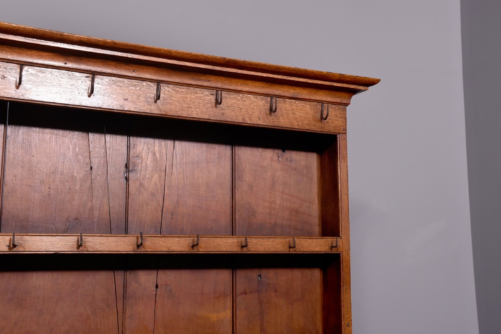 A George III two-part oak dresser featuring an open three-shelf plate rack with iron hooks above two drawers and an open potboard base. View IX