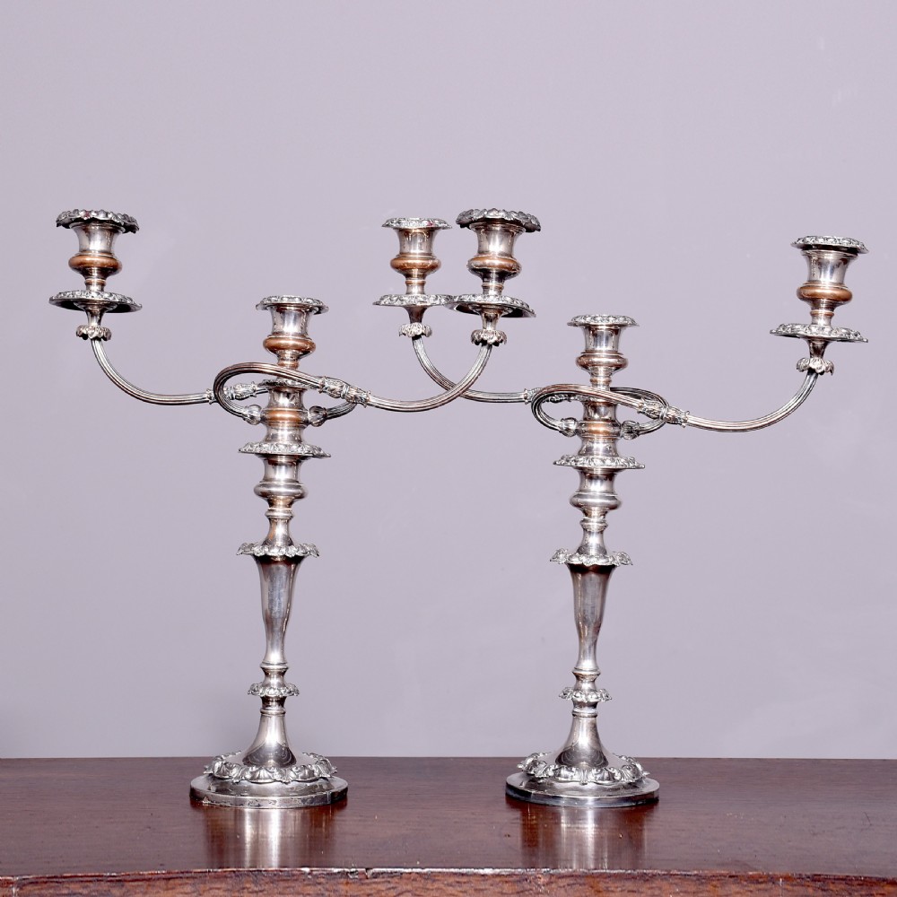 A pair of antique silver-plated three-light candelabra featuring circular bases, baluster stems, and curved reeded branches.