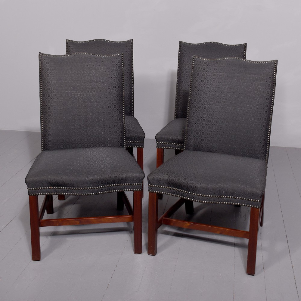 A set of four George III style side chairs upholstered in dark grey patterned fabric with brass stud trimming and straight mahogany legs.