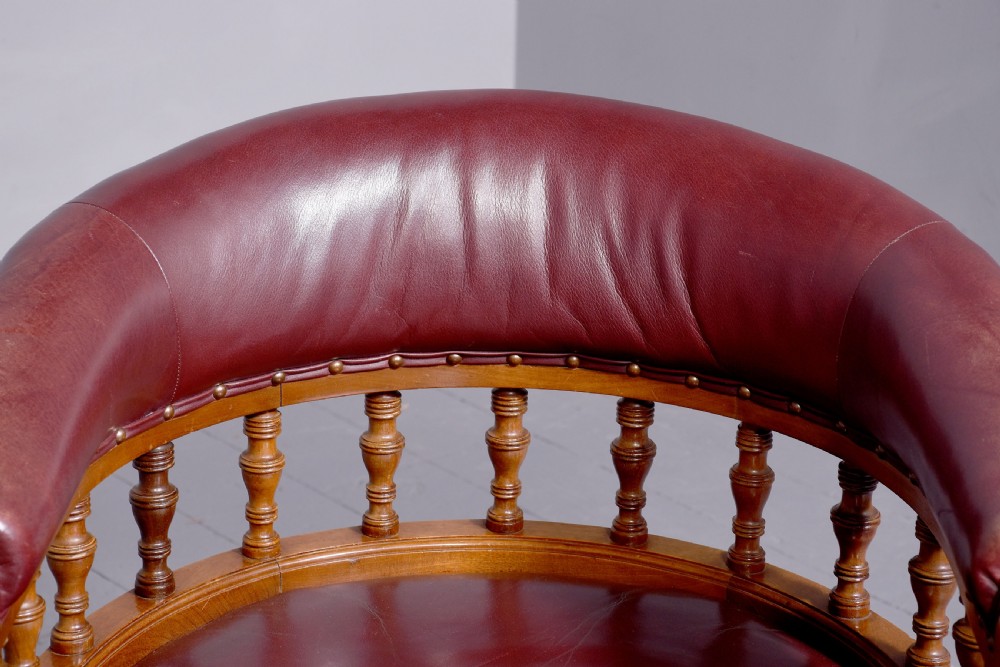 A Victorian walnut desk chair featuring a curved burgundy leather backrest with brass stud detailing, turned spindles, and front turned legs on brass castors. View III