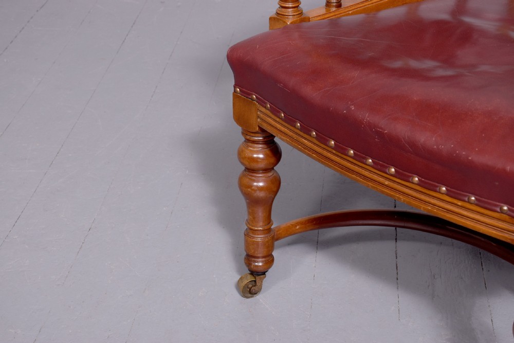 A Victorian walnut desk chair featuring a curved burgundy leather backrest with brass stud detailing, turned spindles, and front turned legs on brass castors. View IV