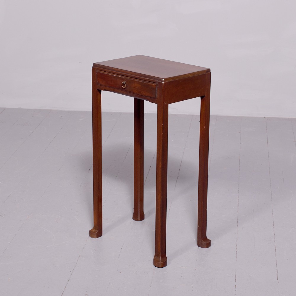 A tall, narrow mahogany side table featuring four straight legs, a single drawer with a central brass ring pull, and a polished wood surface.