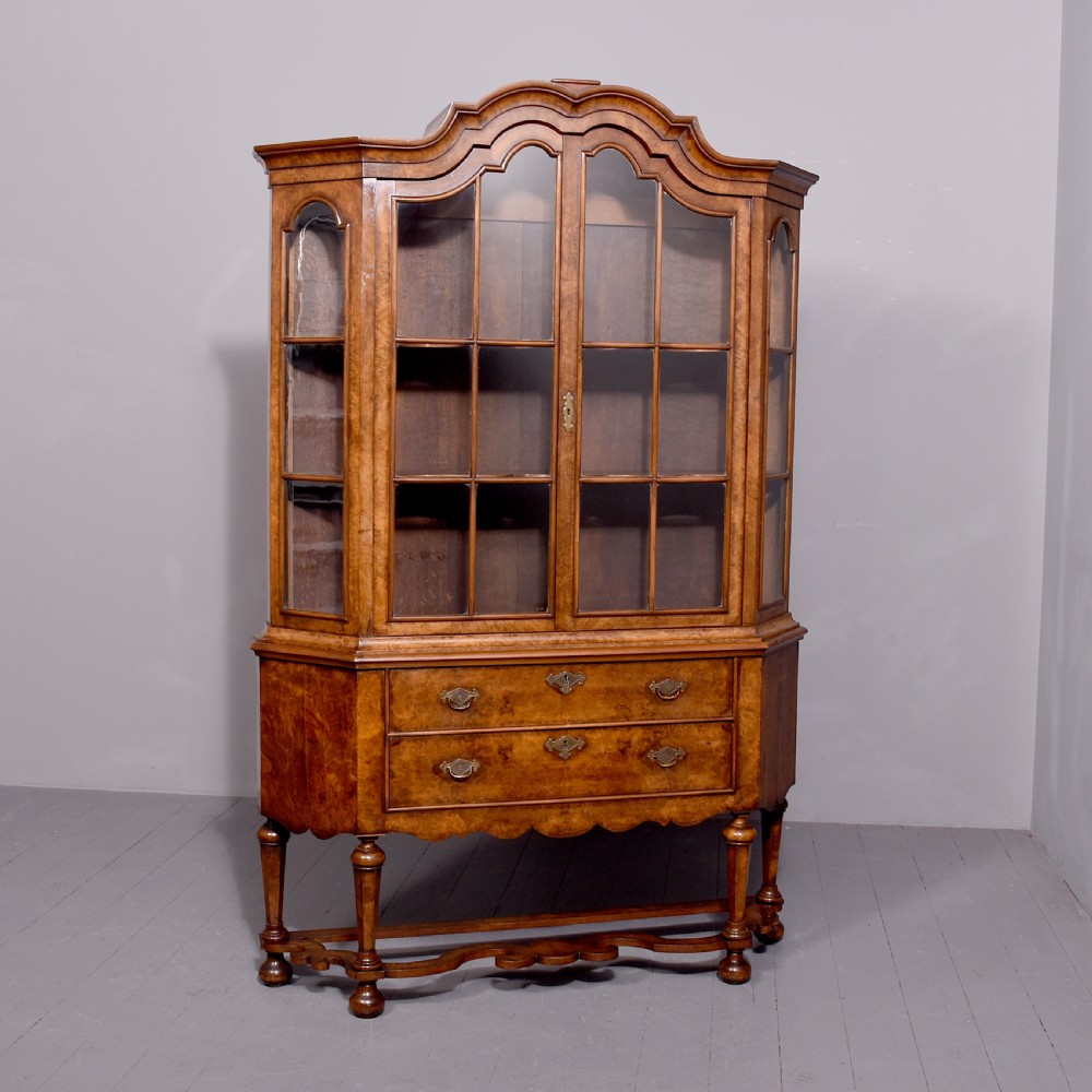 A nineteenth-century Dutch burr walnut display cabinet featuring canted glazed sides, an arched cresting cornice, two lower drawers, and turned legs connected by a shaped stretcher.