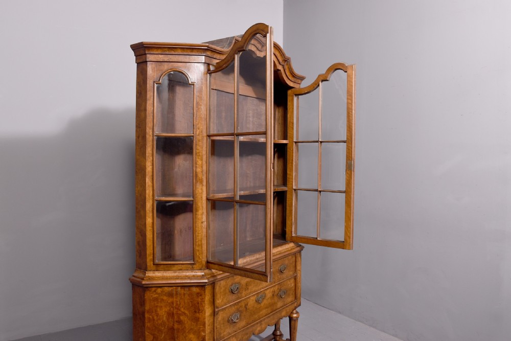 A nineteenth-century Dutch burr walnut display cabinet featuring canted glazed sides, an arched cresting cornice, two lower drawers, and turned legs connected by a shaped stretcher. View X