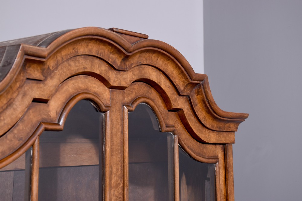 A nineteenth-century Dutch burr walnut display cabinet featuring canted glazed sides, an arched cresting cornice, two lower drawers, and turned legs connected by a shaped stretcher. View XIII