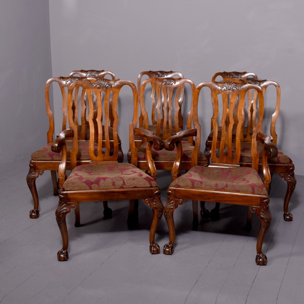 A set of George II style carved walnut dining chairs featuring pierced back splats, cabriole legs with claw and ball feet, and patterned upholstered seats.