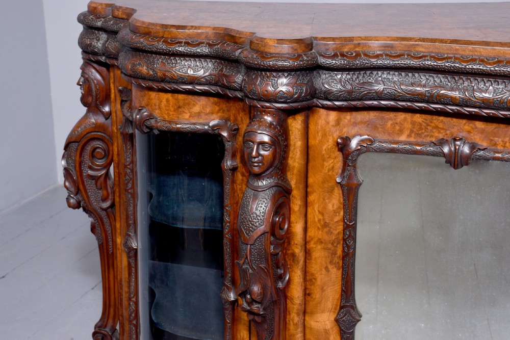 A mid-Victorian burr walnut serpentine-fronted credenza featuring carved female figure pilasters, central mirrored doors, and curved glass side display cabinets. View II