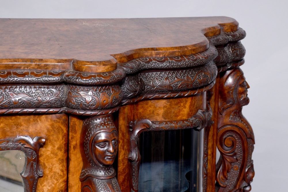 A mid-Victorian burr walnut serpentine-fronted credenza featuring carved female figure pilasters, central mirrored doors, and curved glass side display cabinets. View III