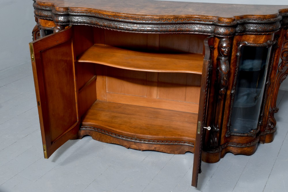 A mid-Victorian burr walnut serpentine-fronted credenza featuring carved female figure pilasters, central mirrored doors, and curved glass side display cabinets. View XI