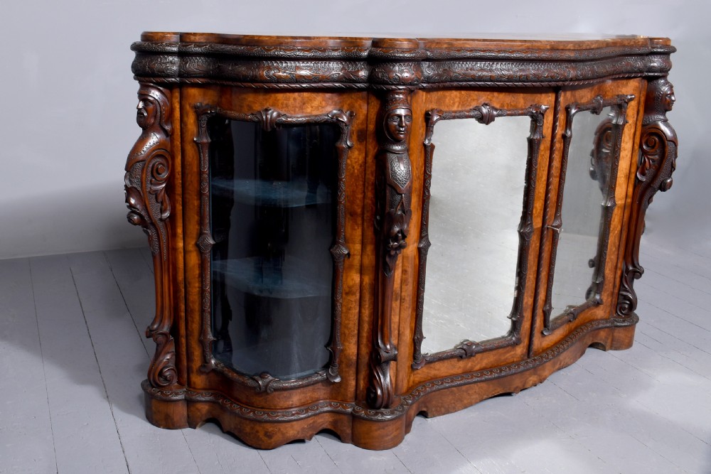 A mid-Victorian burr walnut serpentine-fronted credenza featuring carved female figure pilasters, central mirrored doors, and curved glass side display cabinets. View XIII