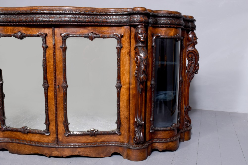A mid-Victorian burr walnut serpentine-fronted credenza featuring carved female figure pilasters, central mirrored doors, and curved glass side display cabinets. View XIV