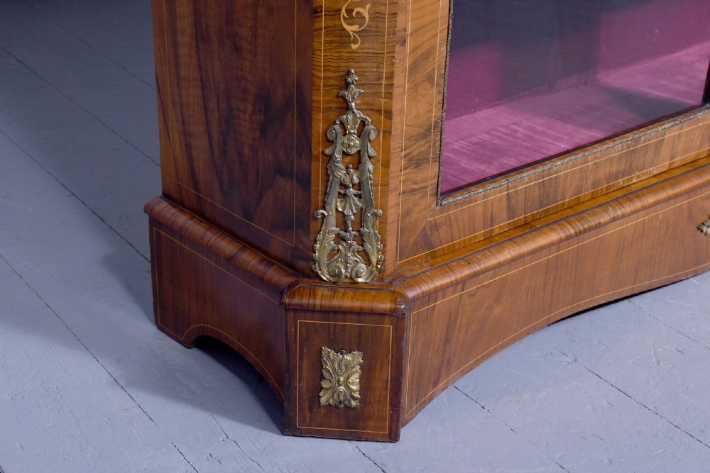 A Victorian figured walnut cabinet featuring twin glazed doors, intricate marquetry floral inlay along the frieze, gilt bronze mounts, and a red fabric-lined interior with three shelves. View VI