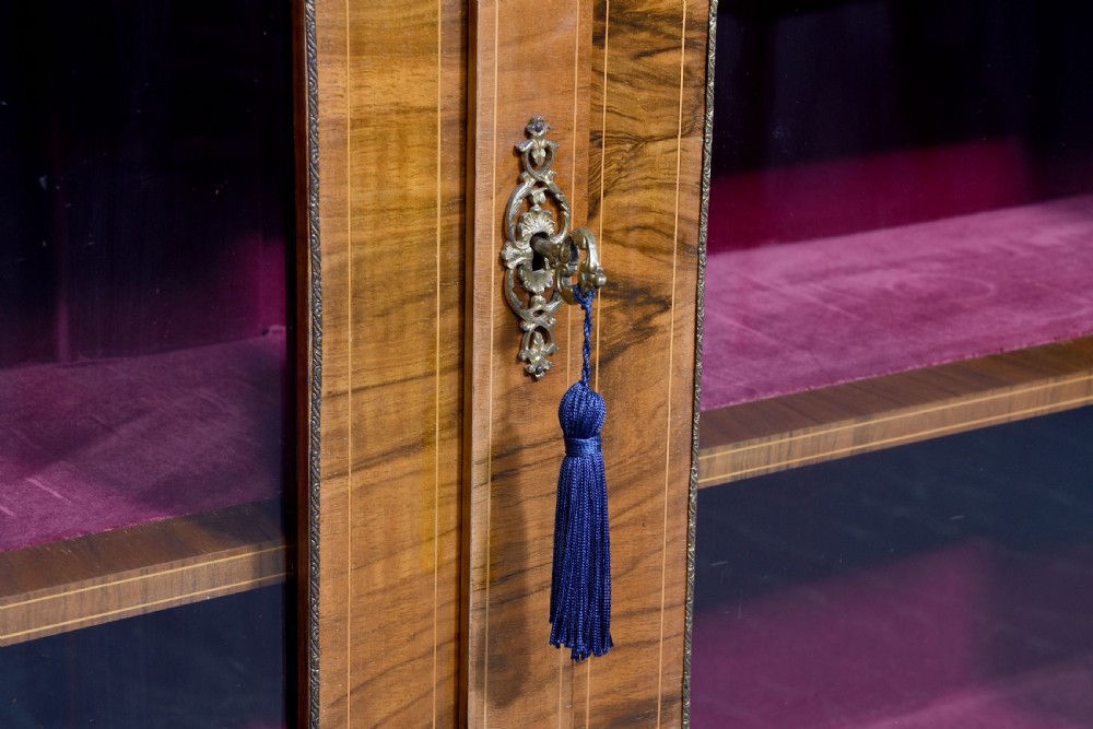 A Victorian figured walnut cabinet featuring twin glazed doors, intricate marquetry floral inlay along the frieze, gilt bronze mounts, and a red fabric-lined interior with three shelves. View VIII